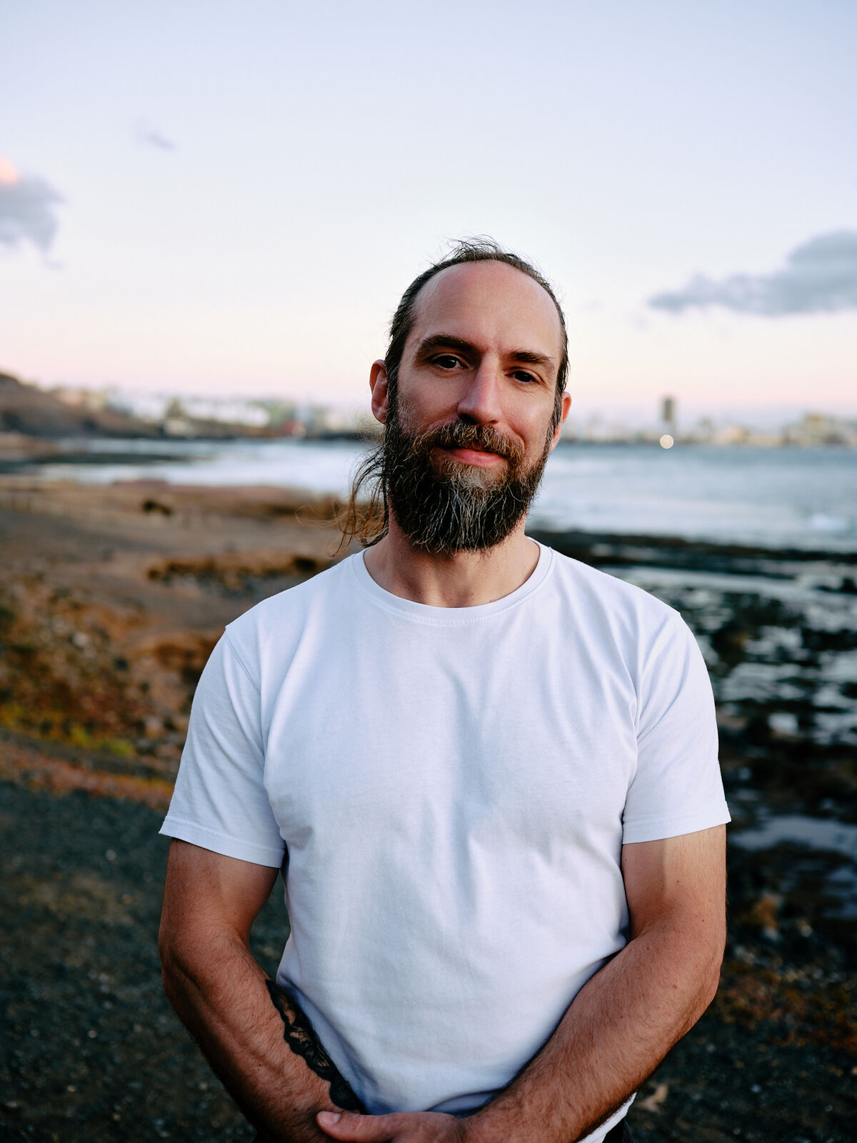 Portrait of Joe at dusk on a rocky coastline, city lights in the distance