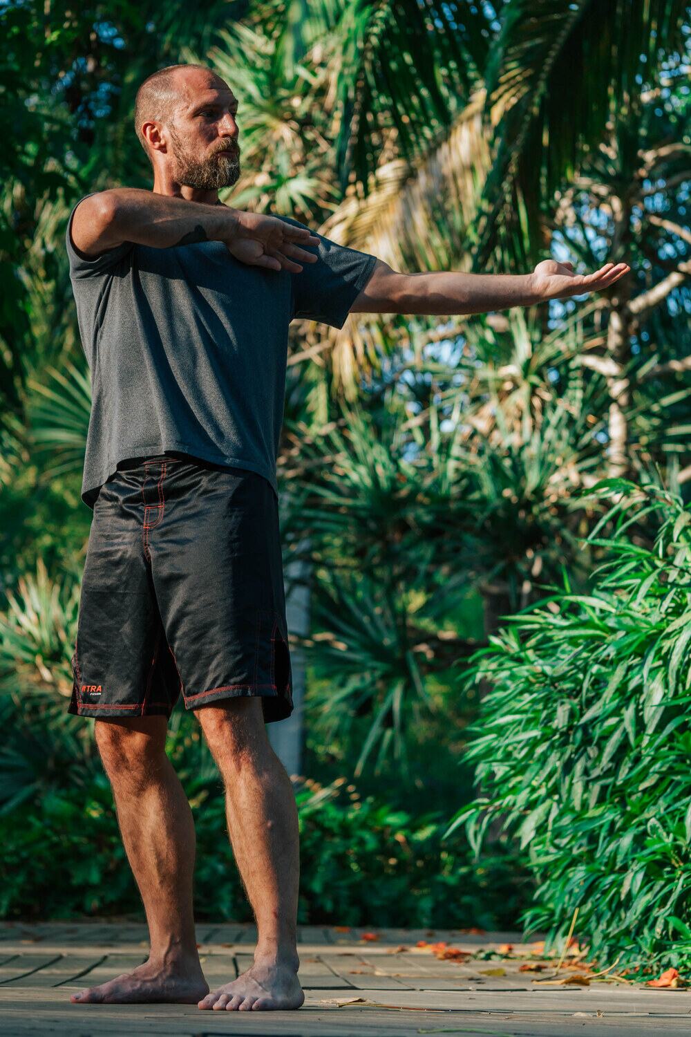 Joe rotating one arm across his body in a standing shoulder mobility drill, outdoors in morning light